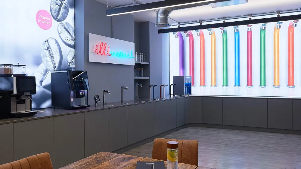 Modern refreshment area with coffee machines on countertop, multiple taps in a row, and colorful illuminated tubes on the wall.